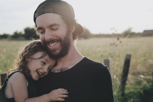 The image depicts a heartwarming moment of a father holding his baby daughter in a field of tall grass. This touching scene illustrates the strong parent-child bond and the importance of nurturing children through various developmental stages.